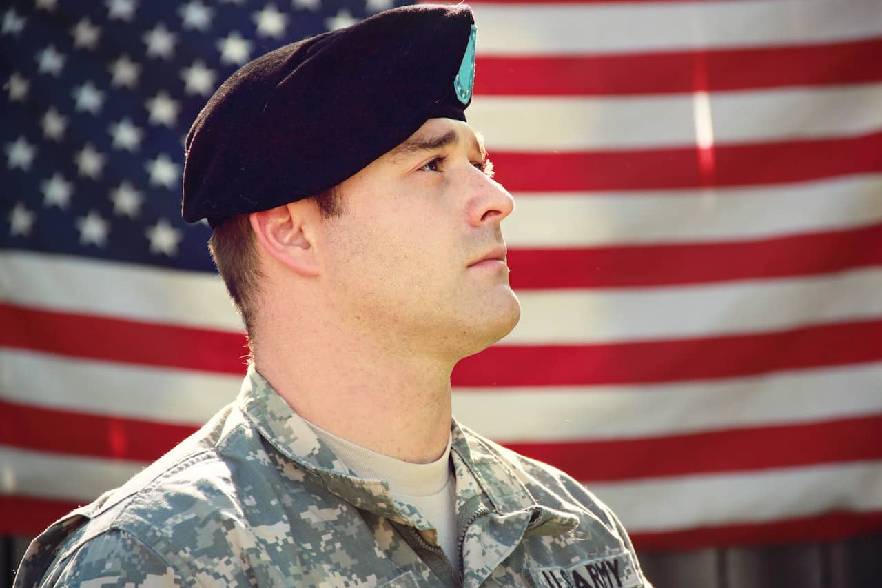 Army member looking to the right with an American flag in the background