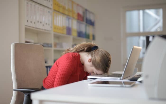 Woman at desk with head resting on keyboard of laptop