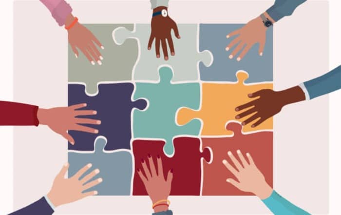 cartoon of multi colored hands reaching for puzzle pieces.