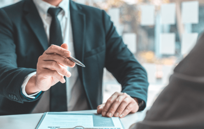 Man is business suit holding pen and sitting at table while interviewing a potential employee