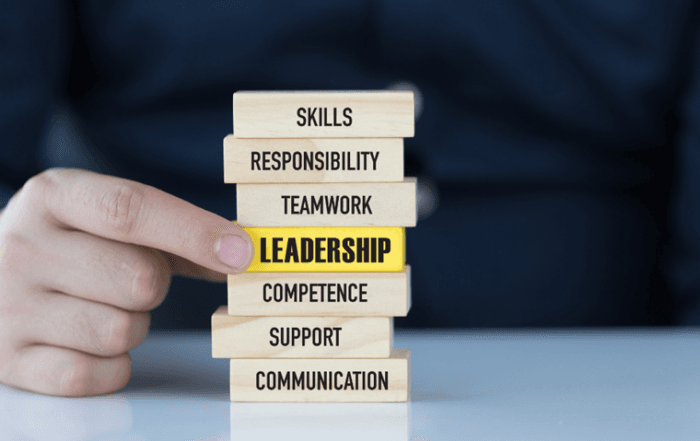 desk with person's hand pointing to a stack of wooden blocks. finger points to the block with the word Leadership.