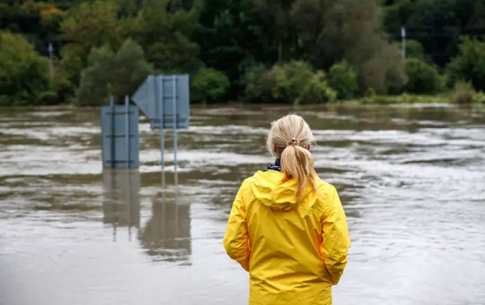 Flooded river. Worried woman looking at overflowing water during flood. Extreme weather and natural disaster