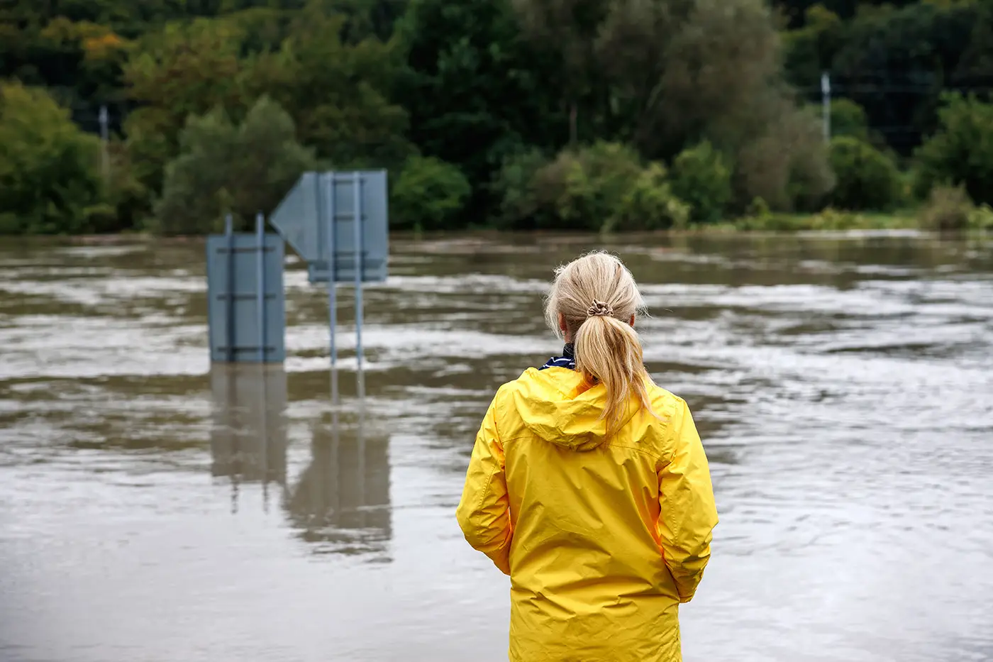 Flooded river. Worried woman looking at overflowing water during flood. Extreme weather and natural disaster